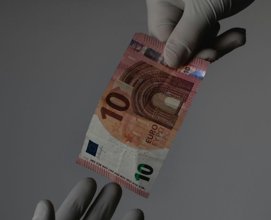 La imagen muestra una mano con guantes que ofrecen alta resistencia y seguridad entregando un billete de 10 euros a otra mano. Representación gráfica de aval financiero.